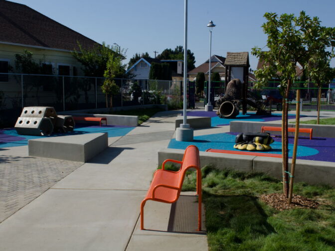 The park contains three play structures with soft, spongy surfaces, benches, and concrete walkways.