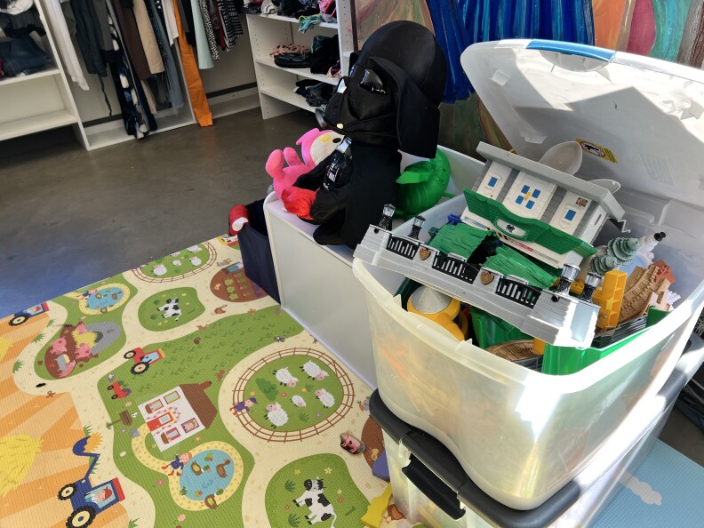 A child's play rug with roads and trucks lays underneath a bin full of donated toys, including a Darth Vader plushie.