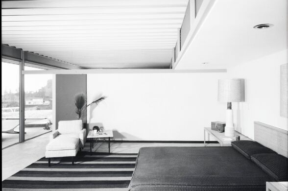 A black and white photo of a bedroom. It has a large bed, and a lounge chair.
