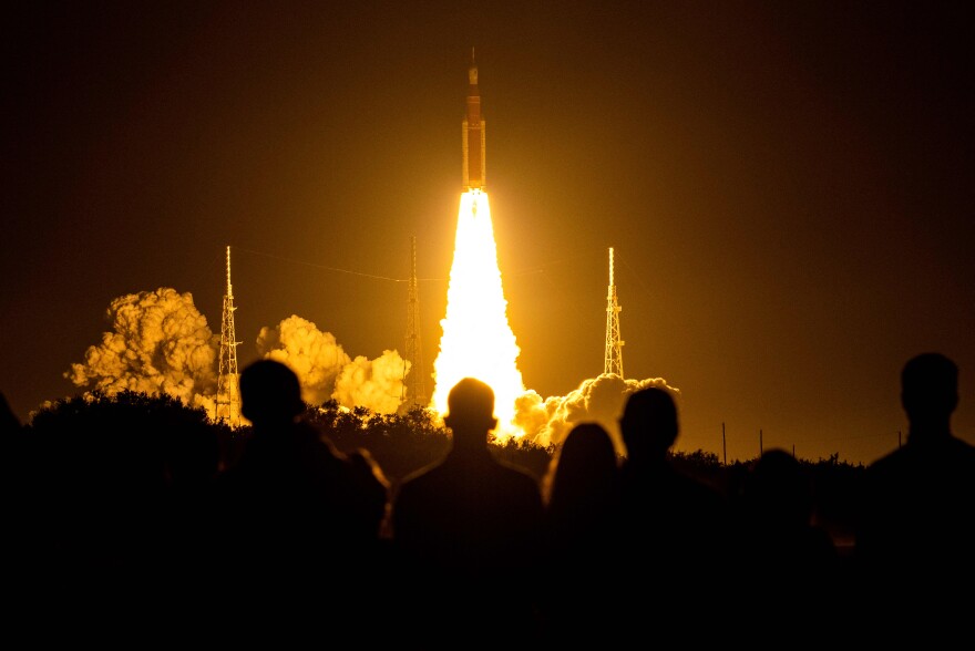 A large plume of fire propels a rocket into the night sky.