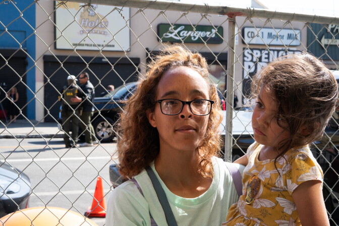 A woman holds her daughter as federal agents stand behind her on the other side of a chain link fence.