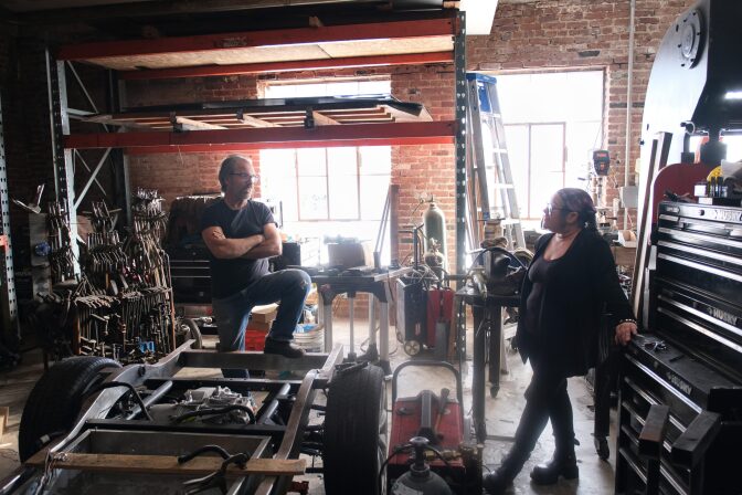 A man and woman stand chatting in a workshop filled with various industrial items