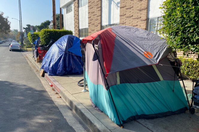 Three tents used by unhoused people are shown on a sidewalk next to an apartment building.
