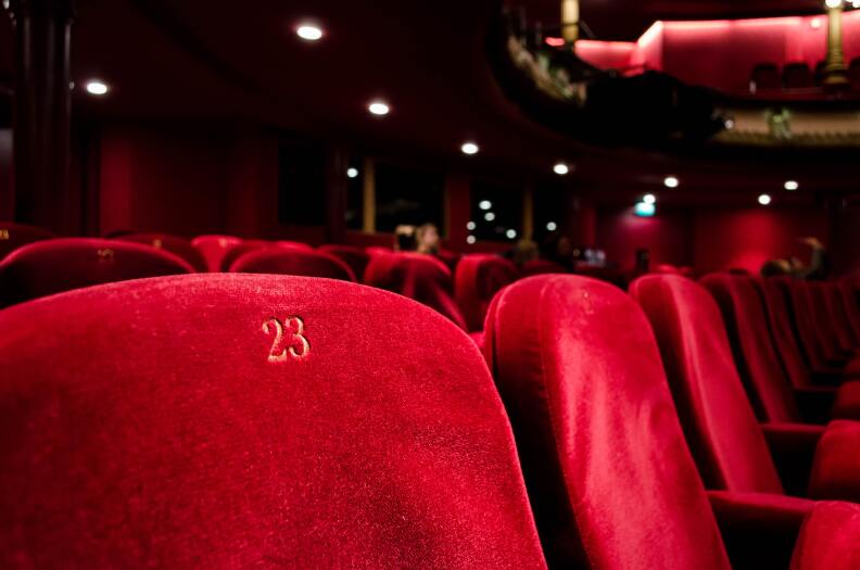 Red, velvety movie theater seats. The one closest to us is numbered 23.