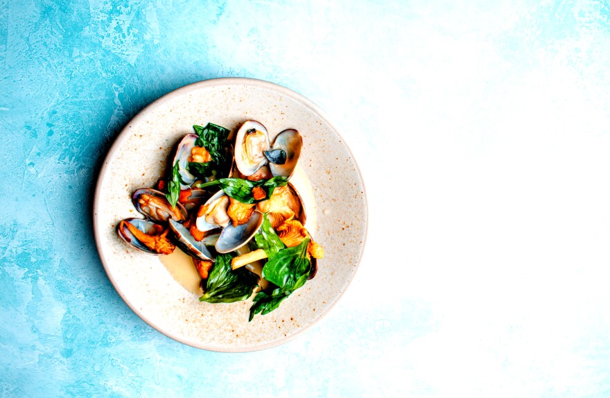 half a dozen cooked mussels on a plate with some green leaves
