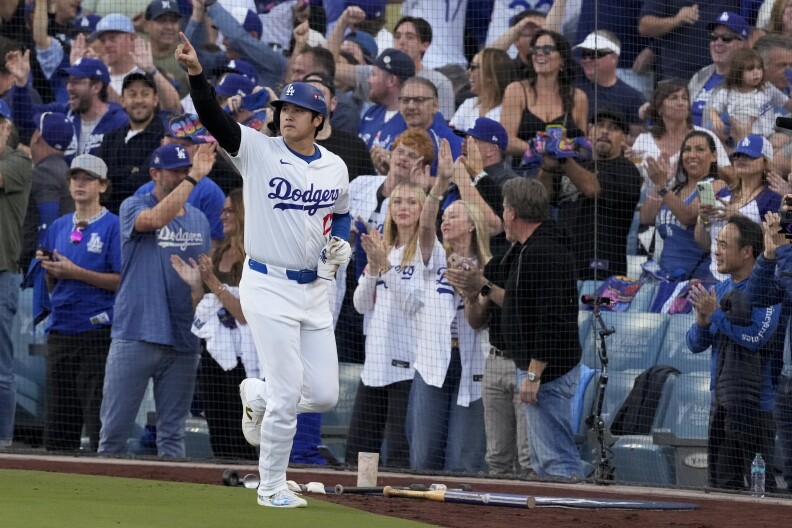 An Asian male in a Dodgers baseball uniform points to the crowd after batting.