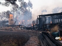 A burned property. At the far right of frame, some planters and pumpkins rest amidst the damage. Fire can be seen burning in the background. 