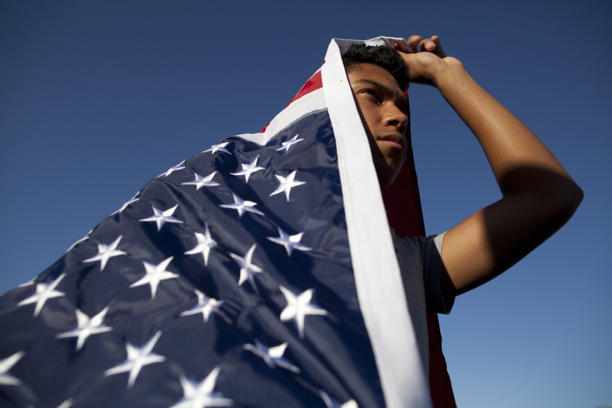 William Bello of Upland is draped in an American flag during a pro-immigration vigil in Murrieta. His family is originally from Mexico City and said that he supports the families coming to the states that are "escaping bad things in South America."
