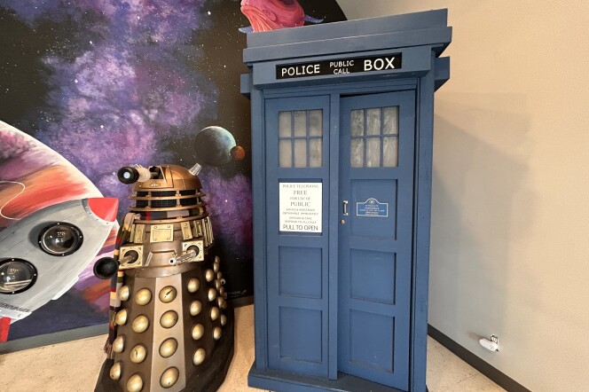 A navy blue police box is displayed next to a mechanical robot in front of a galaxy mural wall.