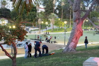 Two paramedics treat a man laying down in the grass. Boys play soccer in the background.