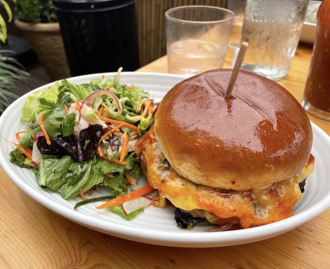 A plate of a burger (with a shiny bun and wooden pin through it) and salad.