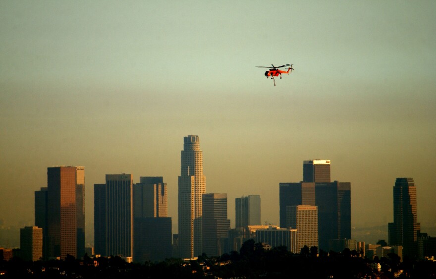 GLENDALE, CA - SEPTEMBER 9:  An Erickson Aircrane firefighting helicopter flies past a slightly smokey downtown Los Angeles skyline as it returns from picking water at an inner-city lake while fighting a wildfire September 9, 2002 in Glendale, California. Homes were threatened today but none were lost in the 800-plus acre wildfire burning in the Los Angeles suburbs of Glendale and Burbank. Containment of the fire is set at 20 percent. (Photo by David McNew/Getty Images)