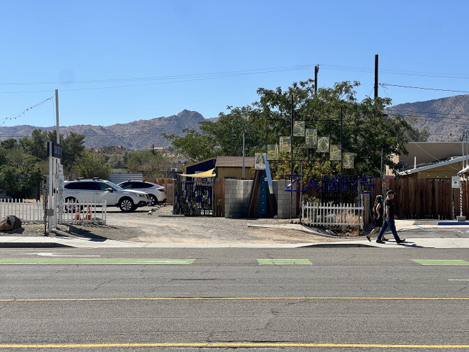 A dirt parking lot off a highway. In the parking lot is a stack of lockers under an A-frame structure.