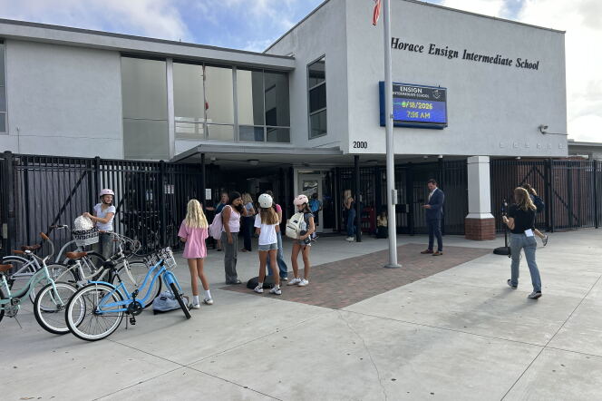 In front of a school building, a group of students stand outside. Three bicycles are parked out front. 