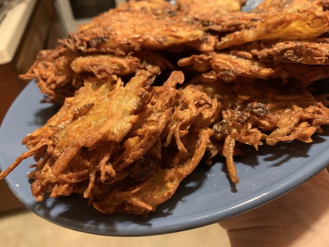 A photograph of a blue plate hoding a pile of crispy brown potato pancakes.