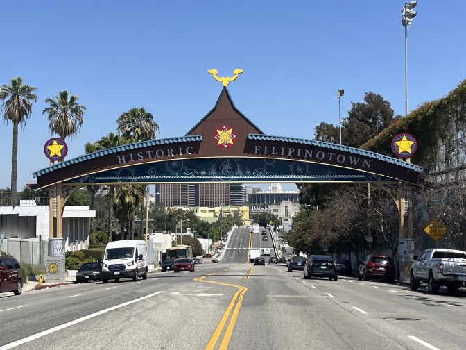 An archway that reads "Historic Filipinotown" spans a four-lane city street with a dozen cars headed in both directions. 
