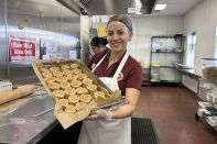 A woman wearing a red polo, apron and hair net holds a baking sheet with freshly rolled cinnamon rolls.
