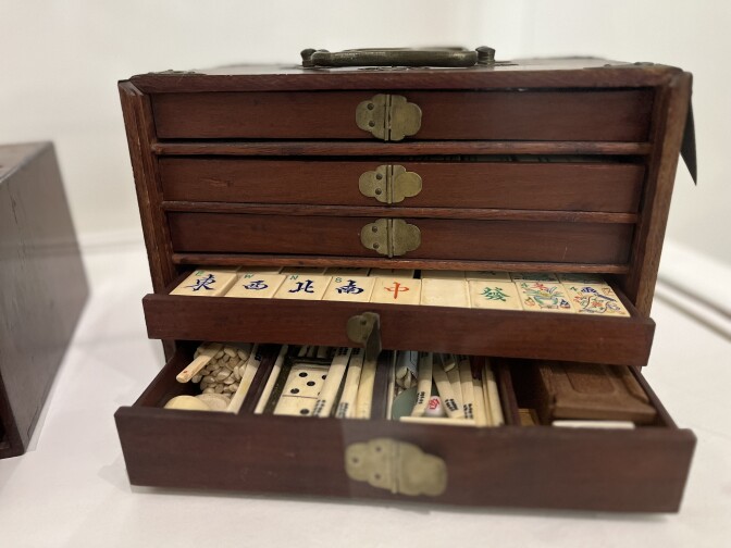 A decades-old wooden mah jong set with shelves oopen to expose tiles and die.