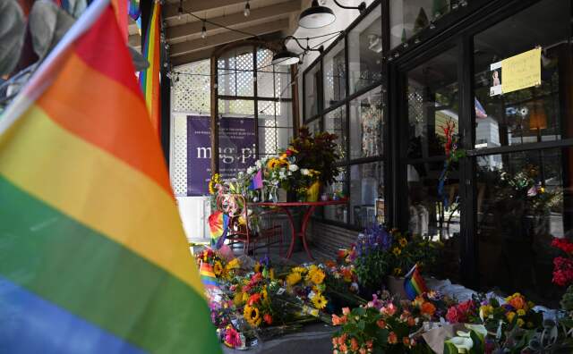 A rainbow flag hands in the foreground. In the background there are bouquets of colorful flowers stacked outside of a clothing store called mag.pi.