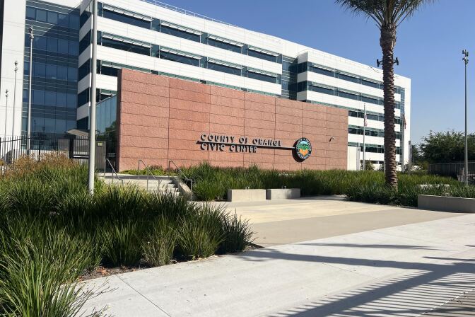 The exterior of a building has a terra cotta-colored stone wall with the words : County of Orange Civic Center and the seal of Orange County.