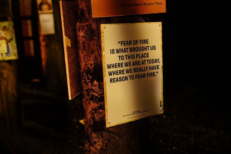 A sign hanging on a tree reads "Fear of fire is what brought us to this place where we are at today, where we really have reason to fear fire."