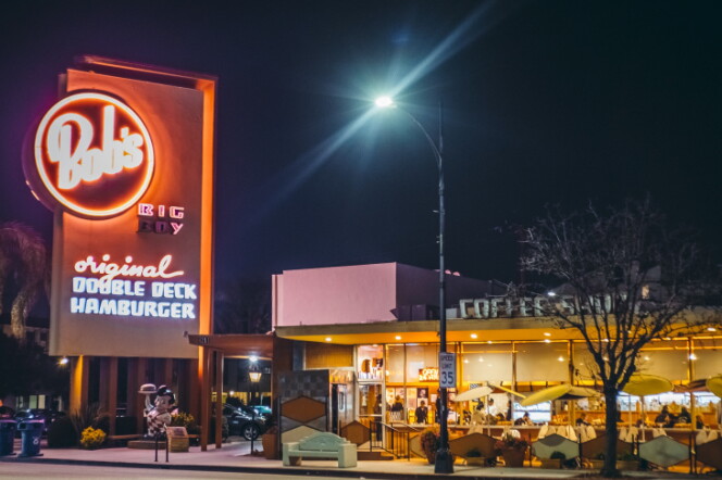 The Bob's Big Boy restaurant in Burbank at night with it's red neon sign illuminated and it's dining space lit up with people inside.