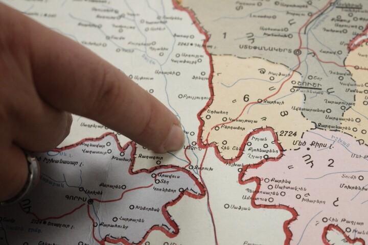 A person's finger points to a spot on a map with red lined borders