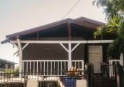 An older, slightly dilapidated two story wooden house painted dark brown with white accents on the front porch.