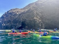 A group of kayakers on their colorful boats in front of a cave near Santa Cruz island.