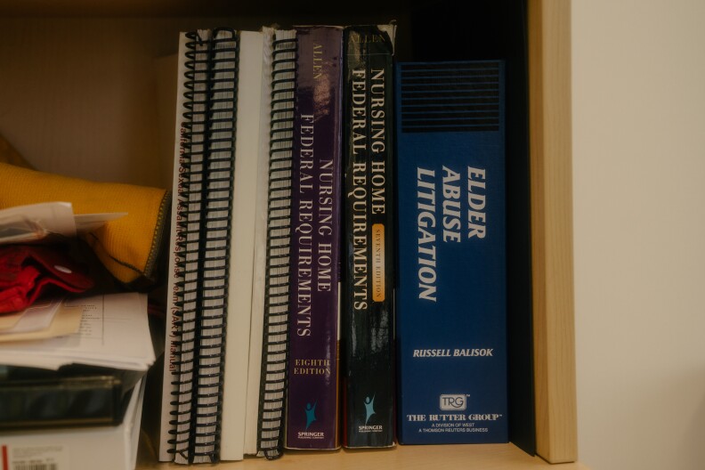 A stack of various books and workbooks in a bookshelf. The books read "Elder Abuse Litigation," and "Nursing Home Federal Requirements." The photo has a purple-hued frame around it.