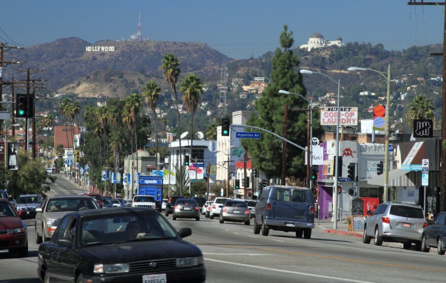 A daytime street scene of Sunset Blvd., with the Hollywood Sign and Griffith Observatory in the distance.