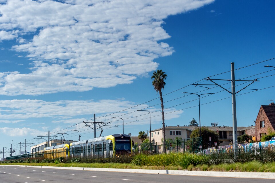 A light rail train running in a neighborhood on a sunny day.
