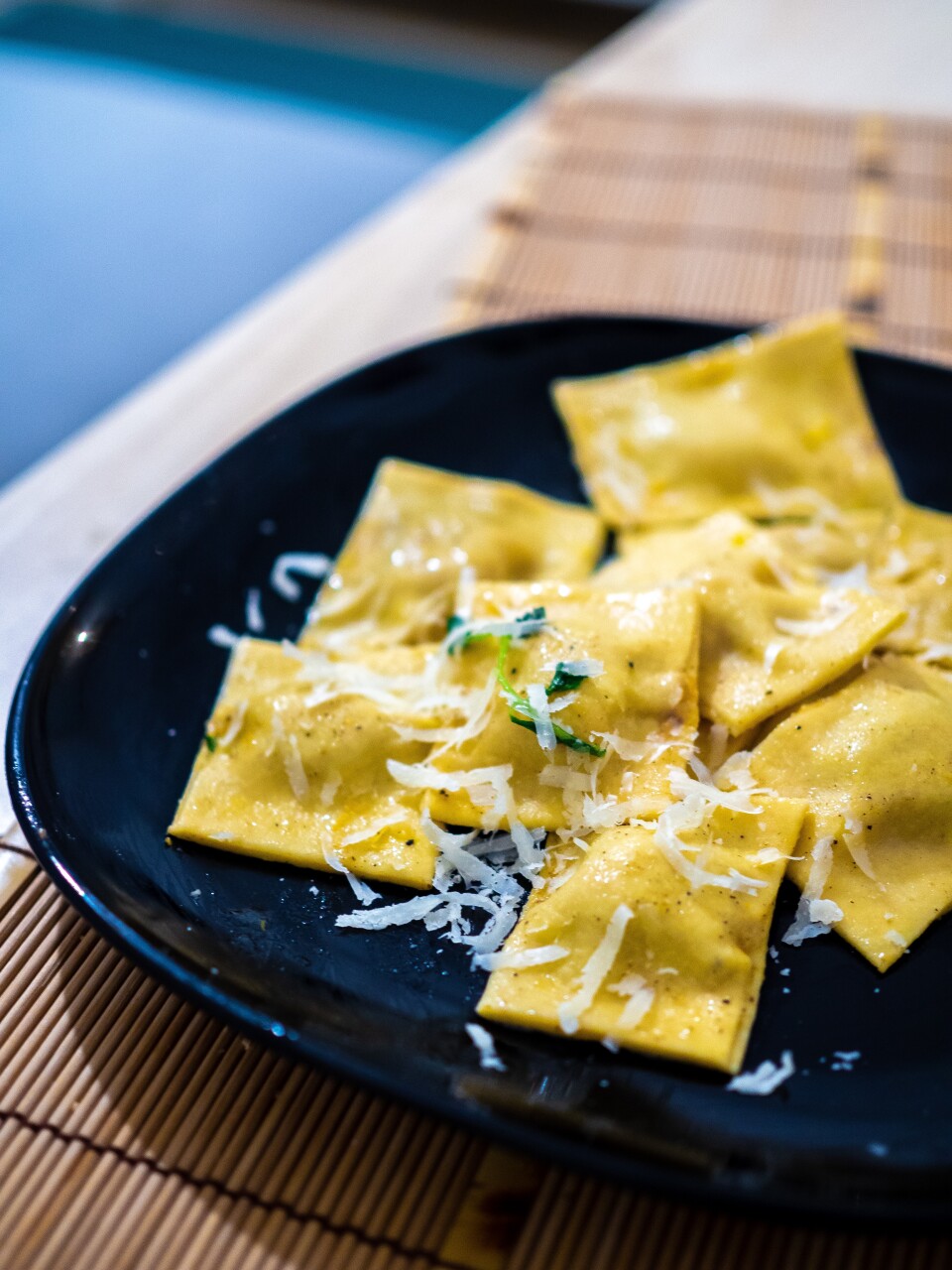 Ravioli with some light cheese shredded over top sits in a black bowl.