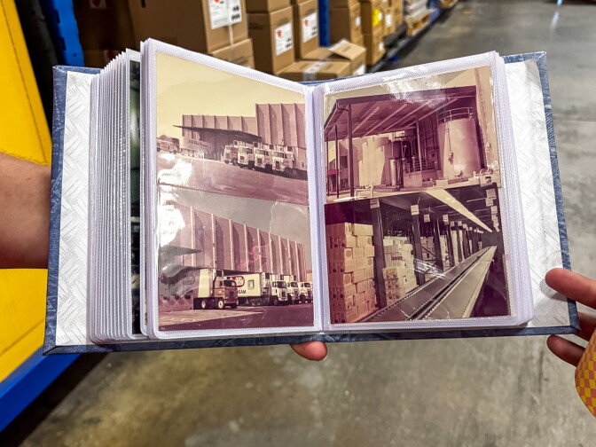 A hand with a light skin-tone holds open a photo album displaying sepia-toned archival photographs of delivery trucks and the interior of the Thrifty Ice Cream plant.