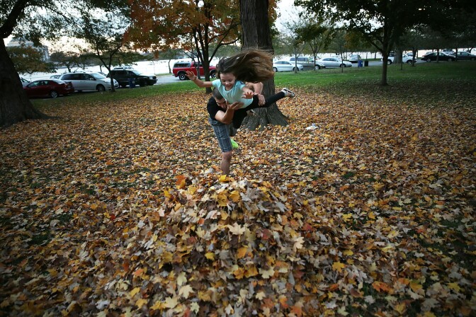 Four-year-old Hailey Bruno plays with her father Joe on a pile of fallen leaves at the Tidal Basin on a warm evening November 6, 2015 in Washington, DC.
