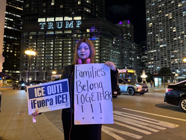 A Latina holds signs reading: ICE Out! iFuera ICE! and Families belong together.