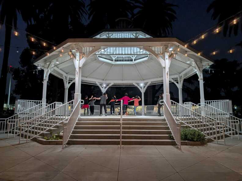 A group of Chinese ladies dancing under a lighted gazebo at night.