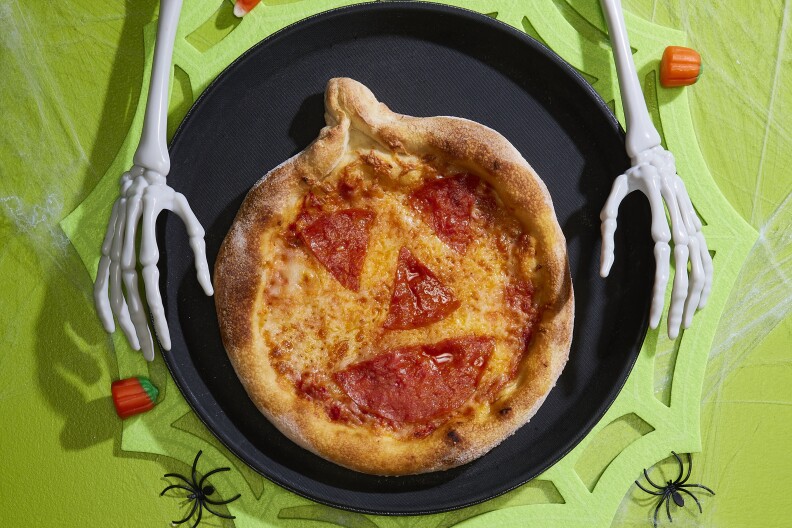 Skeleton arms are holding a black pan with a personal pizza made to look like a jack-o'lantern.