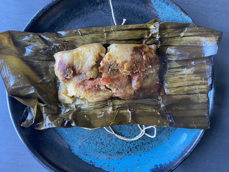 A cooked tamale sits on a banana leaf placed on a blue plate on table
