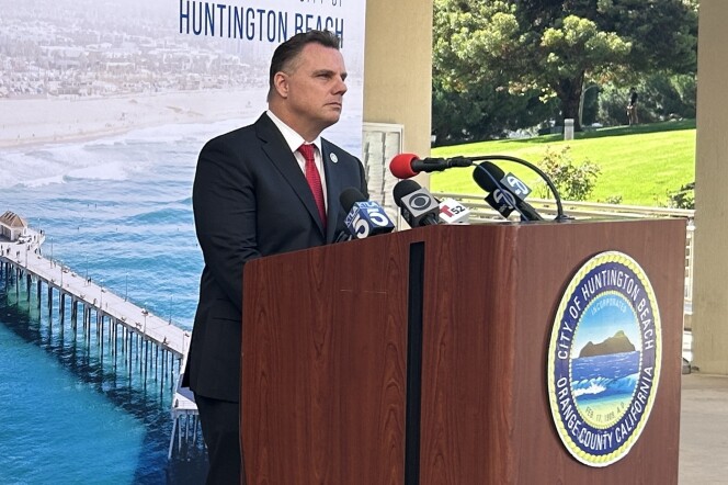 A man at a podium with the seal of the City of Huntington Beach on it and a large image of the pier and the beach behind him.