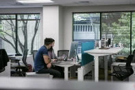 A man and woman sit in an office setting. They are looking at a large, silver computer screen