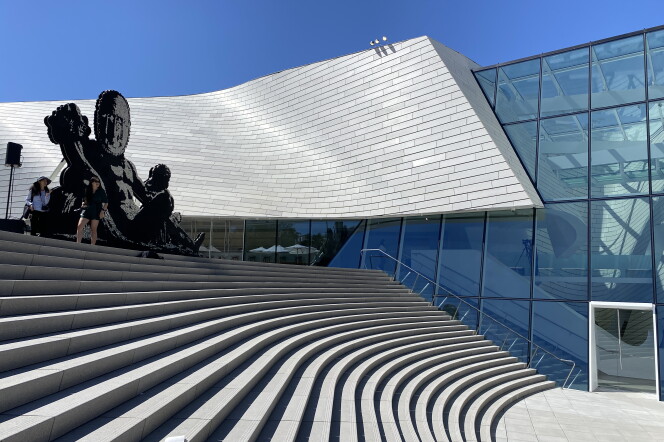 A wide outdoor staircase is in the foreground with the curved, silver-colored sloping roof of a building in the background. 