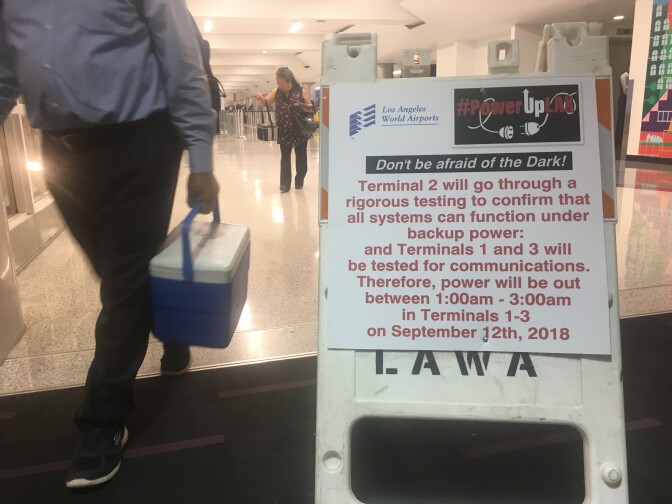 A worker carrying a cooler walks by a placard informing passengers of a power systems test at LAX Terminal 2 early Sept. 12, 2018.