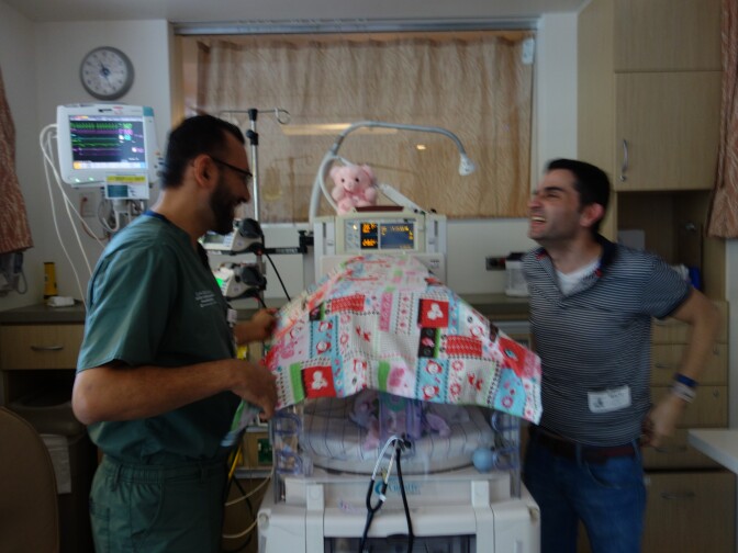 Dr. Antoine Soliman, medical director of the Miller Children's Hospital neonatal intensive care unit with new father Saturnino Izquierdo and baby Francesca in the Isolette under the blanket.