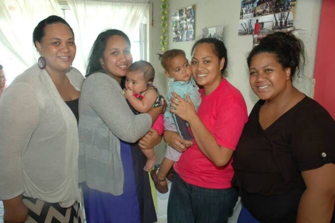 Four smiling Tongan American women. Two women in center are holding babies. 