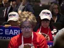 People in a crowd wear hats and pins showing  support of former President Donald Trump.