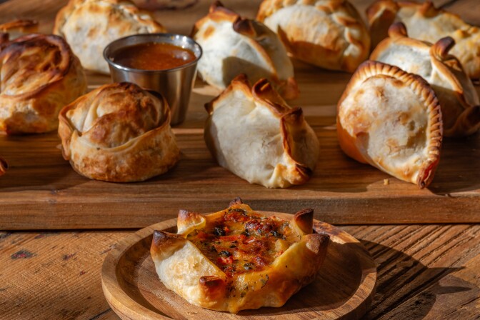 An assortment of empanadas in different shapes and sizes sit on a wooden table