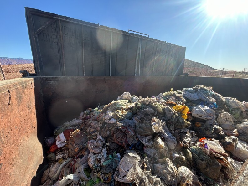 A dumpster full of bagged food waste under a bright sunny sky