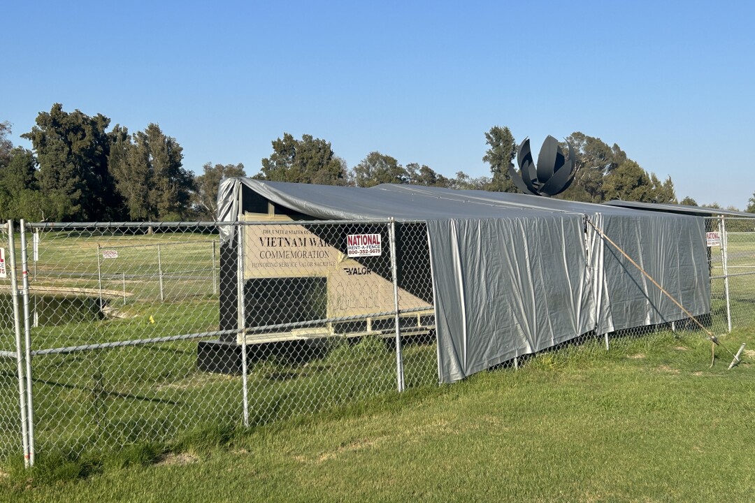 A sign reading Vietnam War commemoration is visible behond a chainlink fence. the structure is draped in silver tarps.