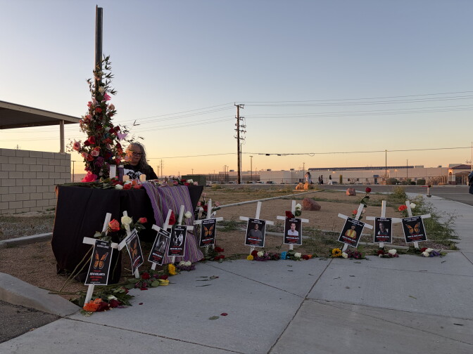 Posters with people's names are affixed to white crosses in the ground next to a makeshift altar.
